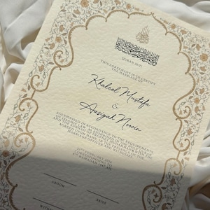 Könnte beinhalten: Elfenbeinfarbene Heiratsurkunde mit einem verzierten goldenen Blumenrand. Das Dokument enthält arabische Schriftzeichen, Namen und Daten. Der Text lautet "Diese Vereinbarung dient zur Bestätigung der Eheschließung von..." und enthält Platz für Unterschriften.