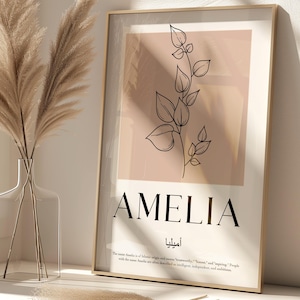 Puede incluir: Un estampado enmarcado con el nombre "AMELIA" en fuente negra, con una ilustración botánica de hojas y tallos. Un jarrón de vidrio transparente contiene hierba de la pampa seca. El estampado tiene un fondo rosa claro.