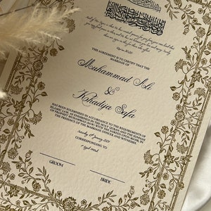 K&ouml;nnte beinhalten: Eine cremefarbene Heiratsurkunde mit goldenen floralen R&auml;ndern und arabischem Text. Der Text lautet: "Dieses Dokument bescheinigt, dass die Ehe von Muhammad Ali & Khadija Safa in &Uuml;bereinstimmung mit den Anforderungen des islamischen Rechts geschlossen wurde, wie es im Heiligen Koran und der Sunna des Propheten Muhammad (SAW) mit dem vereinbarten Mahir festgelegt ist, in Anwesenheit des Standesbeamten und der Zeugen. Samstag, 15. Januar 2029, entsprechend Rajab 1450h".