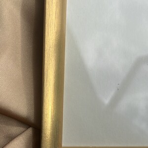 Puede incluir: Un marco de fotos de color dorado con textura de madera. El marco est&aacute; sobre una superficie de tela marr&oacute;n.
