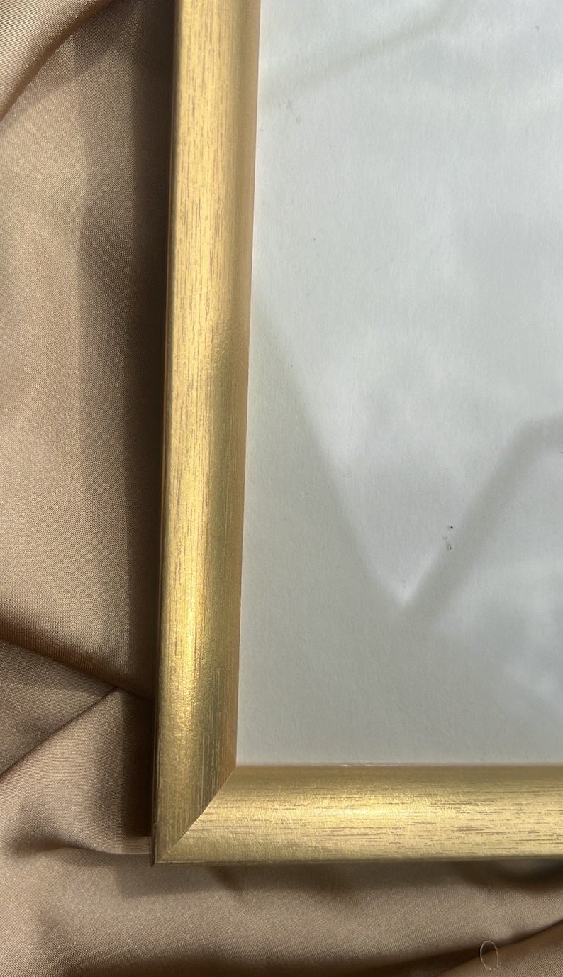 Puede incluir: Un marco de fotos de color dorado con textura de madera. El marco est&aacute; sobre una superficie de tela marr&oacute;n.