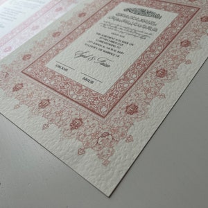 Pode incluir: Um convite de casamento com um design ornamentado, intrincado, vermelho e branco. O texto diz "A cerim&ocirc;nia ser&aacute; realizada no dia [date] &agrave;s [time] em [location], seguida de uma recep&ccedil;&atilde;o em homenagem a [couple's names]" e "Groom & Bride".