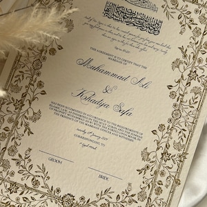 May include: A cream-coloured marriage certificate with gold floral borders and Arabic text. The text reads "This agreement is to certify that the marriage of Muhammad Ali & Khadija Safa has been solemnised in accordance to the requirements of Islamic law, as enshrined in the Holy Quran and the Sunnah of Prophet Muhammad (SAW) with the agreed upon mahr, in the presence of the marriage officer and witnesses. Saturday 15th January 2029, corresponding to Rajab 1450h."
