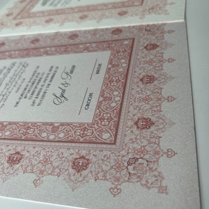 Pode incluir: Um convite de casamento com um design de borda intrincado, ornamentado, de cor marrom-avermelhada. O texto diz "This Agreement...24 Amada Al...Corresponding to...To Certify the Marriage of...Ayed & Fasz...Groom...Bride".