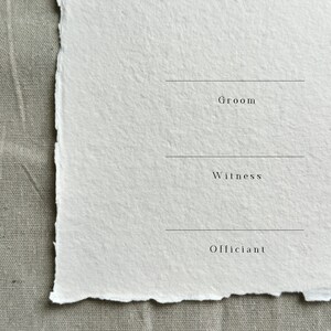 Może przedstawiać: Pusta biała kartka z nadrukowanymi słowami "Groom", "Witness" i "Officiant". Kartka ma szorstką, fakturowaną powierzchnię i prawdopodobnie jest wykonana z ręcznie robionego papieru.