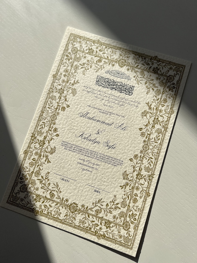 K&ouml;nnte beinhalten: Eine goldfarbene Heiratsurkunde mit verzierten floralen R&auml;ndern. Der Text lautet: "Diese Vereinbarung bescheinigt, dass die Ehe von Muhammad Ali & Khadija Safa in &Uuml;bereinstimmung mit den Anforderungen des islamischen Rechts, wie es im Heiligen Koran und der Sunna des Propheten Muhammad (Friede sei mit ihm) niedergelegt ist, mit dem vereinbarten Mahir in Anwesenheit des Standesbeamten und der Zeugen geschlossen wurde, die dem Br&auml;utigam und der Braut entsprechen."