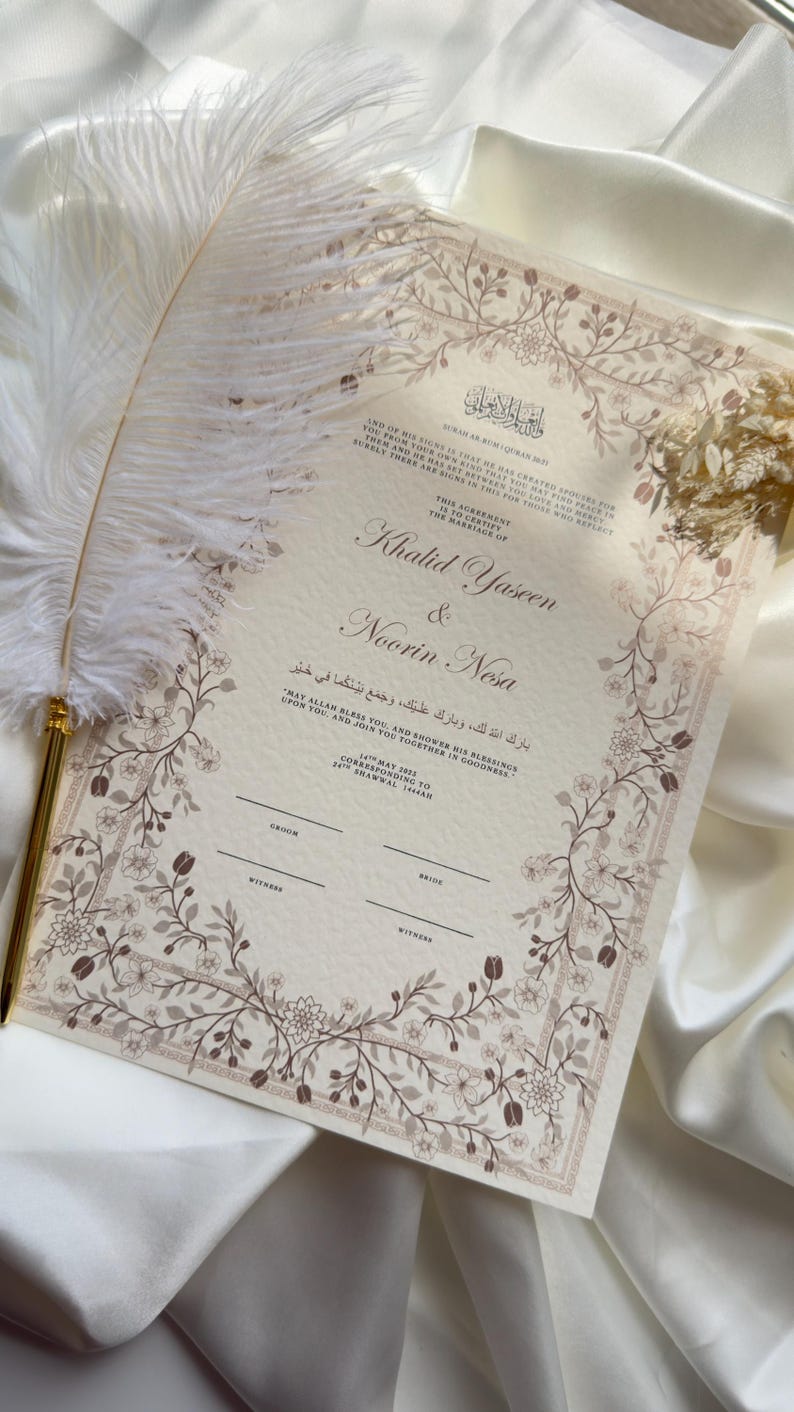 Puede incluir: Un certificado de boda con borde floral y texto en ingl&eacute;s y &aacute;rabe. Los nombres "Khalid Yaseen & Noorin Nesa" se muestran de forma destacada. Una pluma blanca descansa sobre el documento, que est&aacute; sobre una superficie de sat&eacute;n blanco.