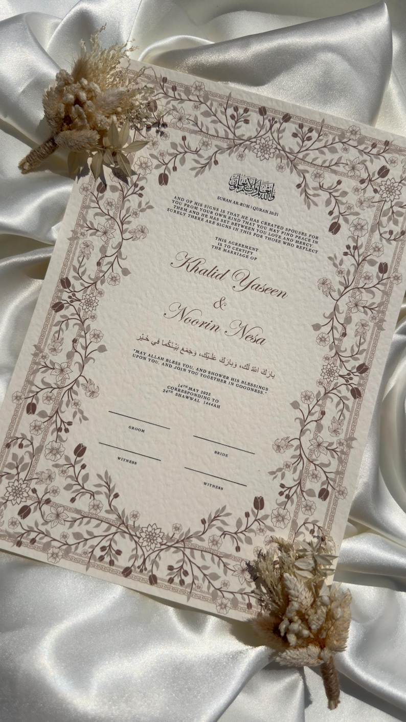 Puede incluir: Un certificado de boda con borde floral y texto. Los nombres "Khalid Yaseen & Noorin Nesa" se muestran de forma destacada. El certificado incluye escritura &aacute;rabe y texto en ingl&eacute;s. Flores secas se colocan cerca del certificado.