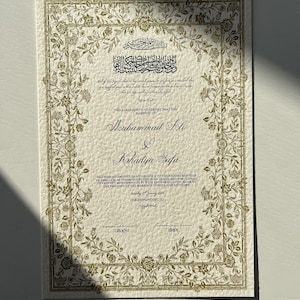 May include: A traditional Islamic marriage certificate with ornate gold floral borders. The text reads "This agreement is to certify that the marriage of Muhammad Ali & Khadija Safa has been solemnised in accordance to the requirements of Islamic Law, as enshrined in the Holy Quran and the Sunnah of Prophet Muhammad (SAW) with the agreed upon mahr, in the presence of the marriage officer and witnesses. Saturday 6th January 2020. Corresponding to..."