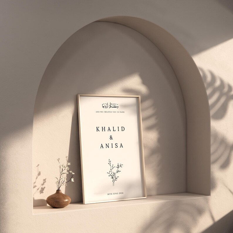 Peut inclure: Une impression encadr&eacute;e avec un fond blanc et du texte noir. Le texte dit "Et nous vous avons cr&eacute;&eacute;s en paires" en &eacute;criture arabe, suivi de la traduction anglaise. Sous le texte figurent les noms "Khalid & Anisa" et la date "16 juin 2024". Une petite illustration florale est centr&eacute;e sous les noms.