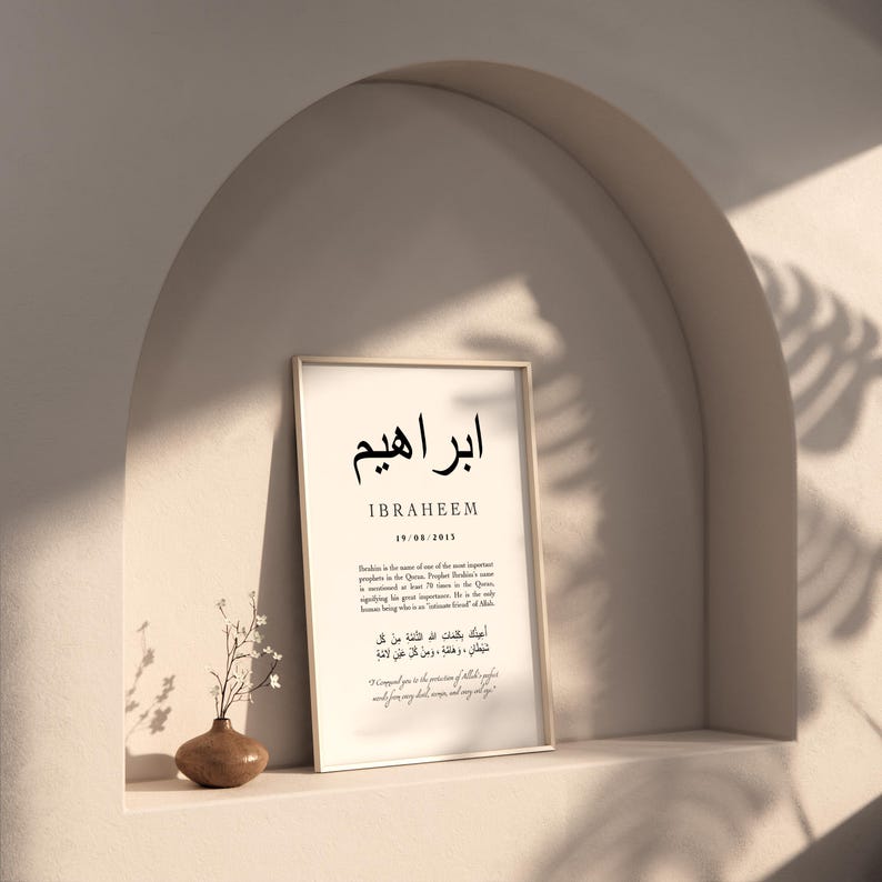 May include: A white framed print with black text. The text includes the Arabic word for Ibrahim, the English spelling of the name, the date 19/08/2013, and a quote in Arabic and English. The print is hanging on a wall with a light brown background.