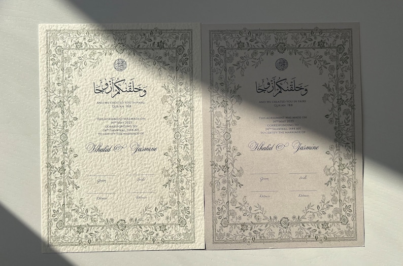 Op de afbeelding: Twee ivoorwitte huwelijkscertificaten met sierlijke bloemranden en Arabische kalligrafie. De tekst luidt "En Wij hebben jullie in paren geschapen" en "Deze overeenkomst is gesloten op 18 mei 2021, overeenkomend met 14 Shawwal 1442 AH, om het huwelijk van Khalid en Jasmine te bevestigen".