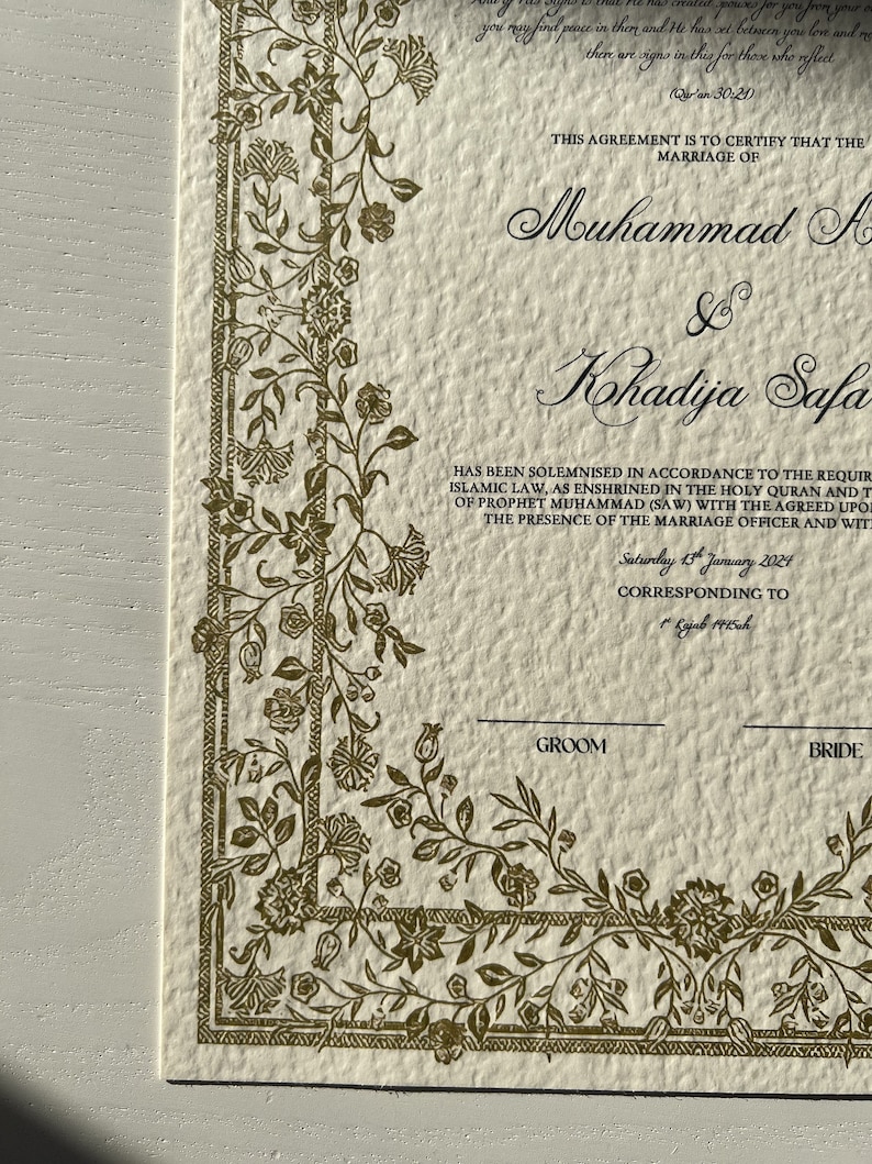 K&ouml;nnte beinhalten: Eine cremefarbene Heiratsurkunde mit einem goldenen floralen Rand. Der Text lautet: "Diese Vereinbarung dient dazu zu bescheinigen, dass die Ehe von Muhammad A & Kohadija Safa in &Uuml;bereinstimmung mit den Anforderungen des islamischen Rechts geschlossen wurde, wie es im Heiligen Koran und den Traditionen des Propheten Muhammad (SAW) verankert ist, mit den vereinbarten Zeugen in Anwesenheit des Standesbeamten und der Zeugen. Samstag, 13. Januar 2024, entsprechend dem 1. Rajab 1445ah."