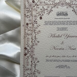 Puede incluir: Un certificado de boda con un dise&ntilde;o de borde floral. El documento presenta texto en ingl&eacute;s y &aacute;rabe, incluyendo nombres, fechas y vers&iacute;culos religiosos. La paleta de colores incluye crema, marr&oacute;n y blanco.