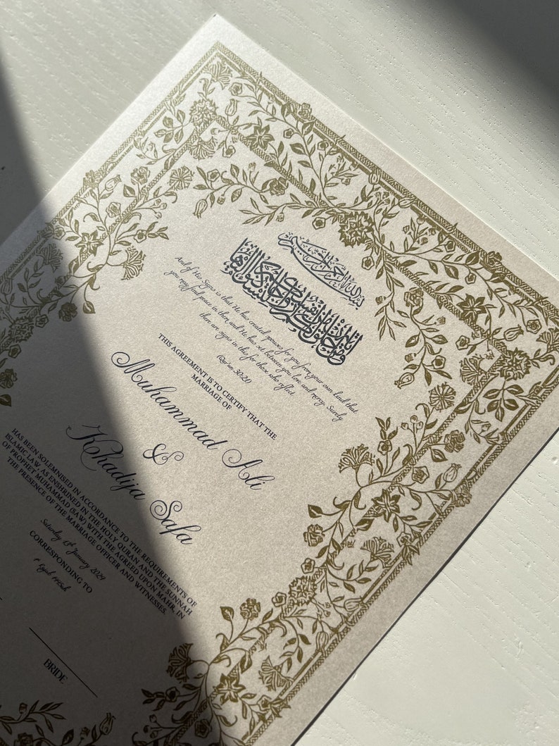 May include: A gold-embossed Islamic marriage certificate with ornate floral borders. The text reads "This agreement is to certify that the marriage of Muhammad Ali & Khadija Safa has been solemnised in accordance to the requirements of Islamic law, as enshrined in the Holy Quran and the Sunnah of Prophet Muhammad (SAW) with the agreed upon mahr, in the presence of the marriage officer and witnesses."
