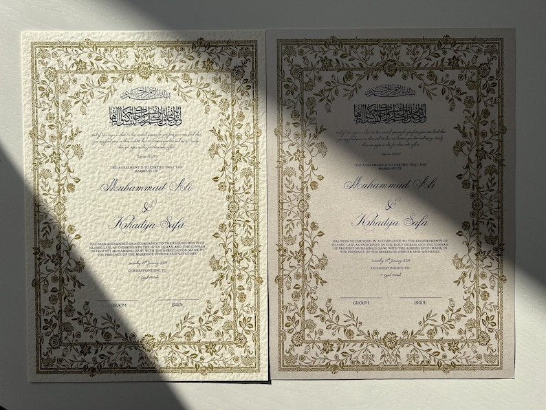 K&ouml;nnte beinhalten: Zwei elfenbeinfarbene Heiratsurkunden mit goldenen floralen R&auml;ndern. Der Text lautet: "Diese Vereinbarung bescheinigt, dass die Ehe von Muhammad Ali und Khadidja Safa in &Uuml;bereinstimmung mit den religi&ouml;sen Riten des Propheten Mohammed (SAW) mit dem Heiligen Koran und der Sunna in Anwesenheit des Standesbeamten und der Zeugen geschlossen wurde. Samstag, 8. Januar 2017. Entspricht dem 7. Jumada Al-Awwal 1438."