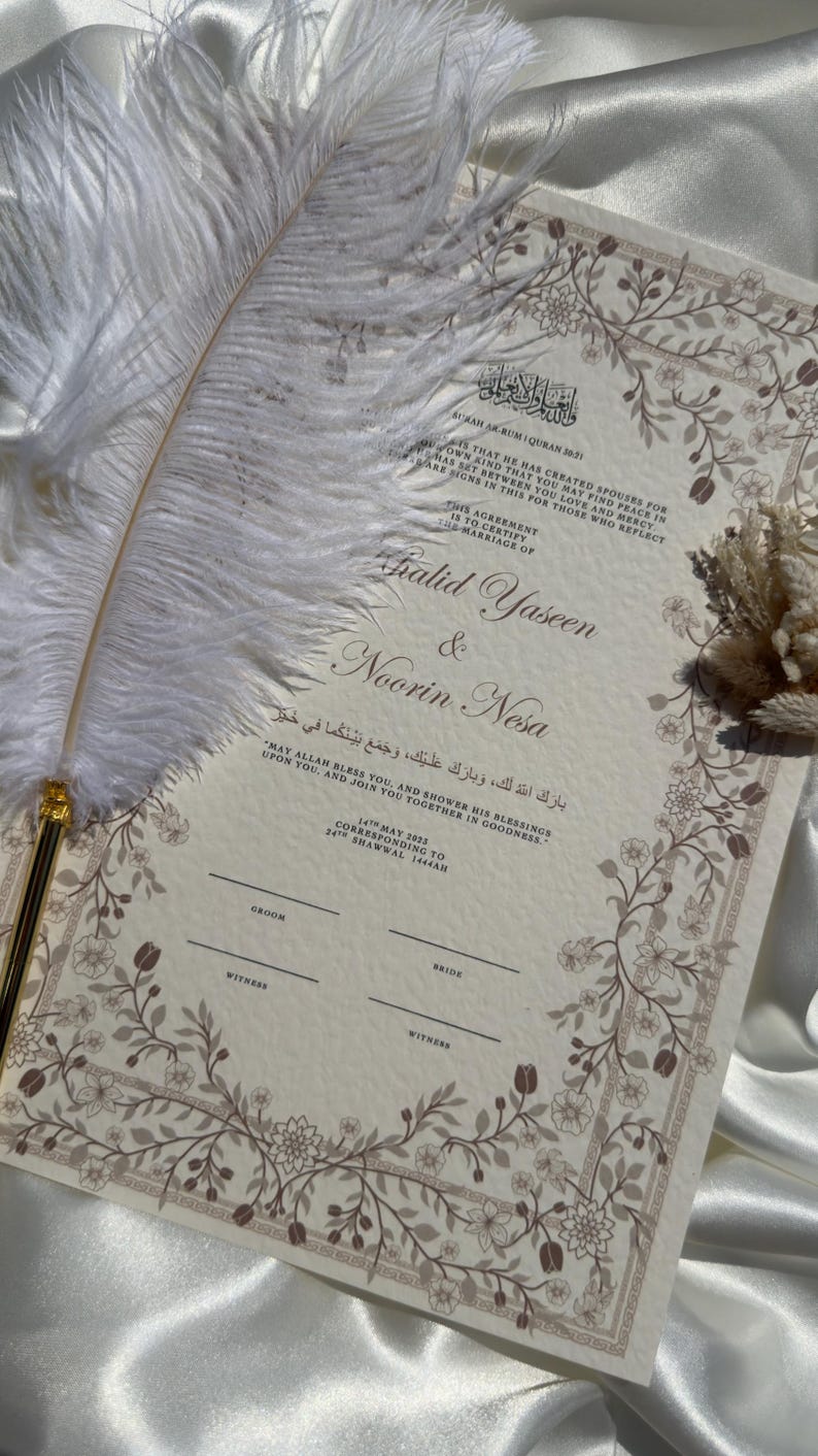 Puede incluir: Un certificado de boda con borde floral y caligraf&iacute;a, con los nombres "Khalid Yaseen & Noorin Nesa." Una pluma blanca descansa sobre el documento, sobre un fondo de sat&eacute;n.