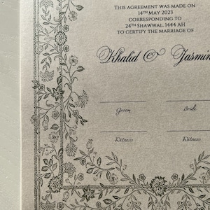 Op de afbeelding: Een beige huwelijkscertificaat met een decoratieve rand van zwarte bloemranken. De tekst luidt "AND WE CREATED YOU IN PAIRS QUR'AN 78:8 THIS AGREEMENT WAS MADE ON 14TH MAY 2023 CORRESPONDING TO 24TH SHAWWAL, 1444 AH TO CERTIFY THE MARRIAGE OF Khalid & Jasmin Groom Bride Witness Witness"