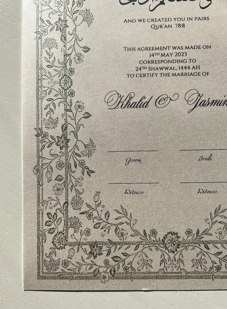 Op de afbeelding: Een beige huwelijkscertificaat met een decoratieve rand van zwarte bloemranken. De tekst luidt "AND WE CREATED YOU IN PAIRS QUR'AN 78:8 THIS AGREEMENT WAS MADE ON 14TH MAY 2023 CORRESPONDING TO 24TH SHAWWAL, 1444 AH TO CERTIFY THE MARRIAGE OF Khalid & Jasmin Groom Bride Witness Witness"