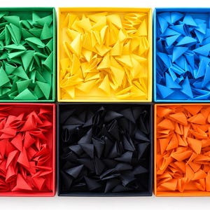 Könnte beinhalten: Sechs quadratische Schachteln in einem Raster angeordnet, jede gefüllt mit zahlreichen kleinen, gefalteten Papierdreiecken. Die Schachteln sind grün, gelb, blau, rot, schwarz und orange, wobei der Inhalt der Farbe der Schachtel entspricht.