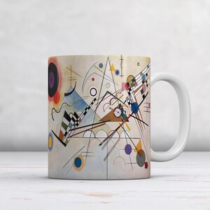 May include: White ceramic mug with an abstract design in the style of Wassily Kandinsky. The design features geometric shapes and lines in colours such as blue, red, yellow, and black. A classic coffee mug.
