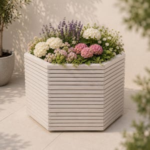 May include: A hexagonal white wooden planter box filled with a vibrant arrangement of white hydrangeas, pink hydrangeas, and purple lavender stalks. The planter features horizontal slats and a clean, geometric design holding various green foliage.