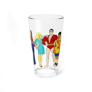 May include: A clear pint glass with a cartoon illustration of four characters. The characters are in various outfits, including a red and yellow superhero costume, a blue dress, and a red jacket with blue trousers. The glass is a standard pint glass.