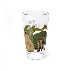 May include: Clear glass pint glass featuring a cartoon illustration of a green dinosaur-like creature and a group of people. The glass has the words "The Land" printed on it.