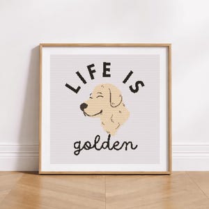 May include: A framed print with the words "LIFE IS golden" in black script and block letters. The image features a smiling, light-tan dog head. The frame is a light brown color, and the background is a light gray.