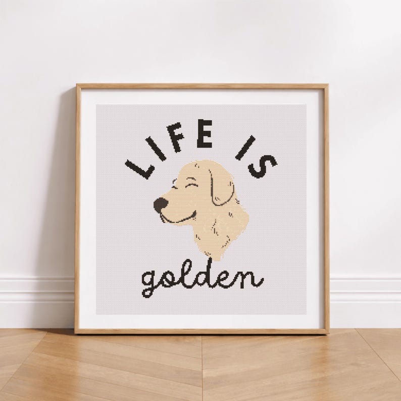 May include: A framed print with the words "LIFE IS golden" in black script and block letters. The image features a smiling, light-tan dog head. The frame is a light brown color, and the background is a light gray.