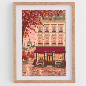 Könnte beinhalten: Ein gerahmter Pixel-Art-Druck, der das Café Sacher mit roter Markise, warmer Innenbeleuchtung und Außenbestuhlung zeigt. Die Szene umfasst eine mehrstöckige Gebäudefassade, einen großen Baum mit herbstlichem Laub und am Boden verstreute Blätter.