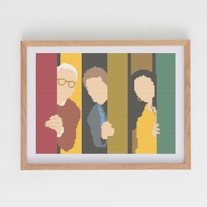Puede incluir: Una obra de arte en punto de cruz enmarcada con tres figuras en un estilo minimalista. Las figuras están divididas por bloques de color verticales rojos, amarillos, negros y verdes. La obra está en un marco de madera marrón claro.