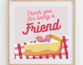 May include: A framed cross-stitch art piece with the text "Thank you for being a Friend" above a slice of cheesecake topped with strawberries and blueberries. The cheesecake sits on a red and white checkered tablecloth.