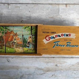 May include: A wooden box of picture cubes depicting the story of Goldilocks and the Three Bears. The box is open and the cubes are arranged in a grid pattern. The box lid features the title "Picture Cubes Goldilocks and the Three Bears" in colourful lettering.