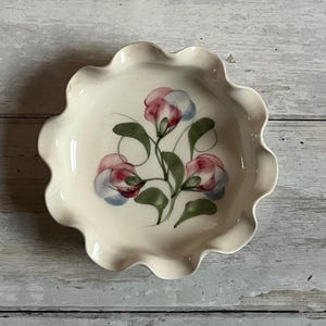 May include: A white ceramic pie dish with a scalloped edge. The dish features a hand-painted design of pink and blue sweet pea flowers with green leaves.