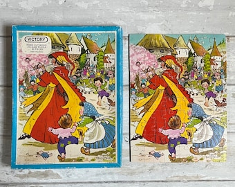 May include: A vintage jigsaw puzzle box with a colorful illustration of a group of children in a village setting. The box is labeled "Victory Hand Cut Wood Jig Saw Puzzle 80 Pieces".
