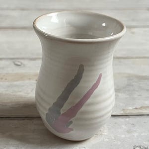 Può includere: Un vaso in ceramica bianca con un'apertura svasata e un fondo arrotondato. Il vaso presenta un design astratto rosa e grigio.