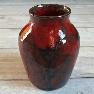 May include: A handmade ceramic vase with a glossy finish. The vase has a deep red glaze with black marbling, creating a unique pattern. The rim is a darker shade of brown. This decorative vase is suitable for displaying flowers or as a standalone art piece.