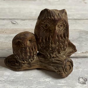 May include: A brown, carved wooden sculpture of two owls perched on a branch. The owls have detailed feather and eye carvings. The sculpture is a decorative item, likely for home decor.