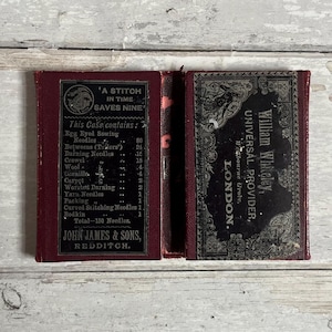 Op de afbeelding: Een rood leren naai-naaldendoosje met een lijst van de meegeleverde naalden: 80 naalden met oog, 24 tussennaalden (kleermakers), 15 stopnaalden, 15 borduurnaalden, 4 wollen naalden, 4 gienille-naalden, 2 tapijtnaalden, 2 wollen stopnaalden, 1 garennaald, 1 verpakkingsnaald, 1 gebogen steeknaald en 1 stopnaald. Het doosje is gelabeld met "A Stitch in Time Saves Nine" en "John James & Sons, Redditch". De andere kant van het doosje is gelabeld met "William Whiteley, Universal Provider, Bourne Grove, London."
