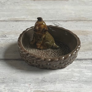 May include: A brown ceramic dog figurine sitting inside a brown ceramic basket with a woven pattern.