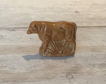 May include: A brown ceramic figurine of a cow with a calf. The figurine is made by Wade England.