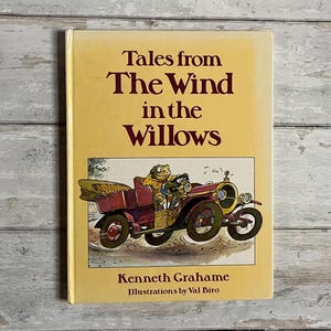 May include: A yellow book cover with the title "Tales from The Wind in the Willows" by Kenneth Grahame. The cover features an illustration of a frog driving a red car.