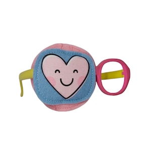 May include: Pink and blue plush toy with a smiling heart on the front and a pink and yellow ring handle.