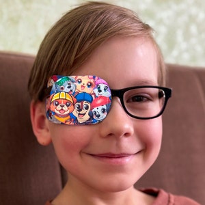 Può includere: Un bambino con gli occhiali e una benda per l'occhio colorata con personaggi dei cartoni animati. La benda ha un elastico nero ed è progettata per coprire un occhio.