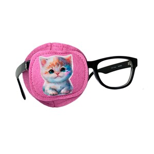 Può includere: Un cerotto per l'occhio rosa con un simpatico design di gattino dei cartoni animati. Il cerotto per l'occhio è attaccato a un paio di occhiali con montatura nera.