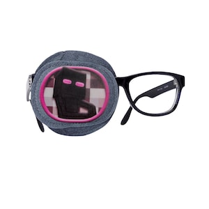 Puede incluir: Un parche para el ojo gris con un diseño de Creeper de Minecraft rosa y negro. El parche para el ojo está unido a unas gafas con montura negra.