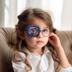 Op de afbeelding: Een jong meisje draagt een bril met een blauw ooglapje met een Paw Patrol-ontwerp. Het ooglapje is zacht en comfortabel voor kinderen.