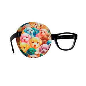 Puede incluir: Un parche para el ojo negro con un estampado colorido de muchos cachorros. El parche para el ojo está unido a unas gafas con montura negra.