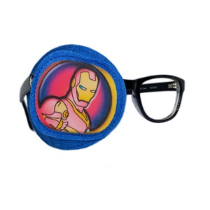 Puede incluir: Parche para el ojo azul con una imagen colorida de Iron Man. El parche para el ojo está unido a un par de gafas con montura negra.